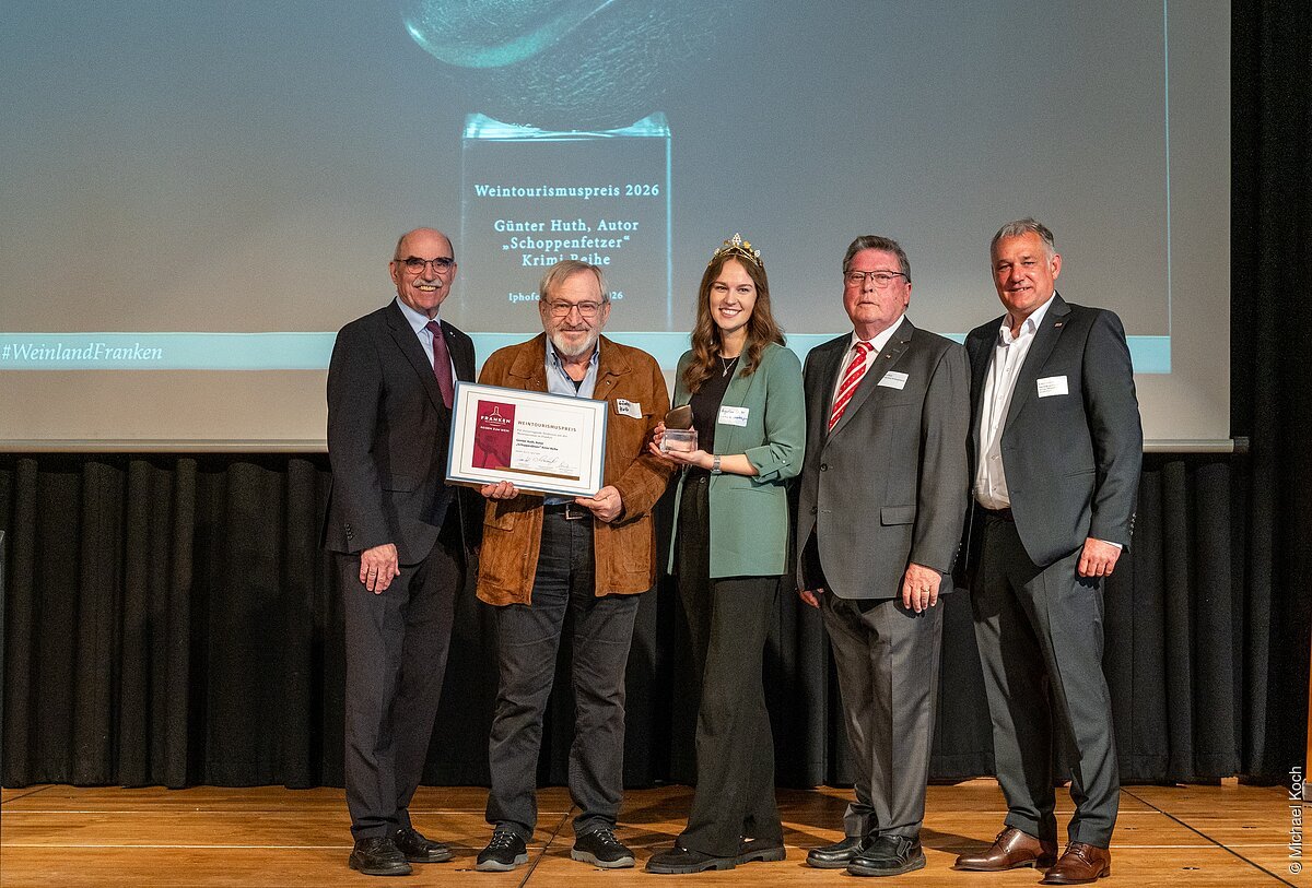 Fünf Personen stehen auf Bühne, eine hält Urkunde, eine hält Pokal, im Hintergrund Projektion mit Text Weintourismuspreis 2026.